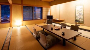 Une pièce de style japonais traditionnel, avec un sol recouvert de tatamis, une petite table basse avec des coussins, un téléviseur et une porte coulissante.