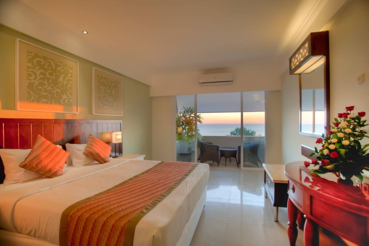 Une chambre d’hôtel avec un grand lit, un bureau et une vue sur le coucher de soleil sur l’océan.