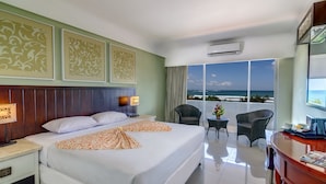 Ein Hotelzimmer mit einem großen Bett, einem Schreibtisch mit Stuhl, einem kleinen Tisch mit einer Vase und Blick auf den Ozean.