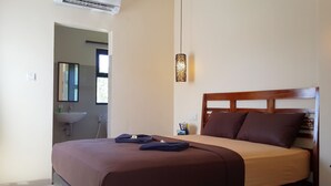 Una camera da letto con un letto, un comodino, una lampada da parete e un bagno visibile attraverso una porta aperta.