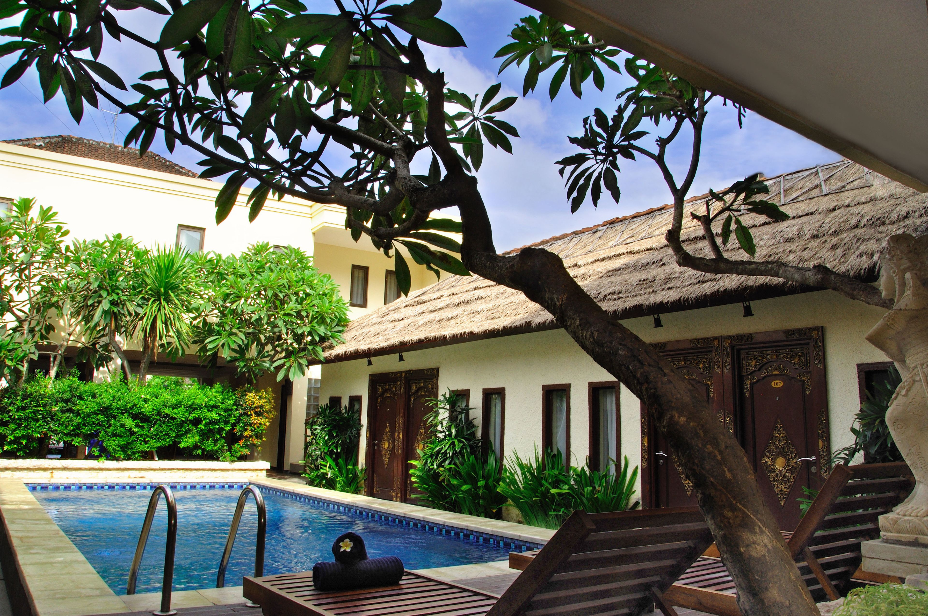 A pool area with a thatched-roof building, lounge chairs, and lush greenery.