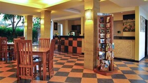 Un'hall d'albergo con pavimento a scacchi, sedie di legno, una reception e una bacheca informativa a parete.