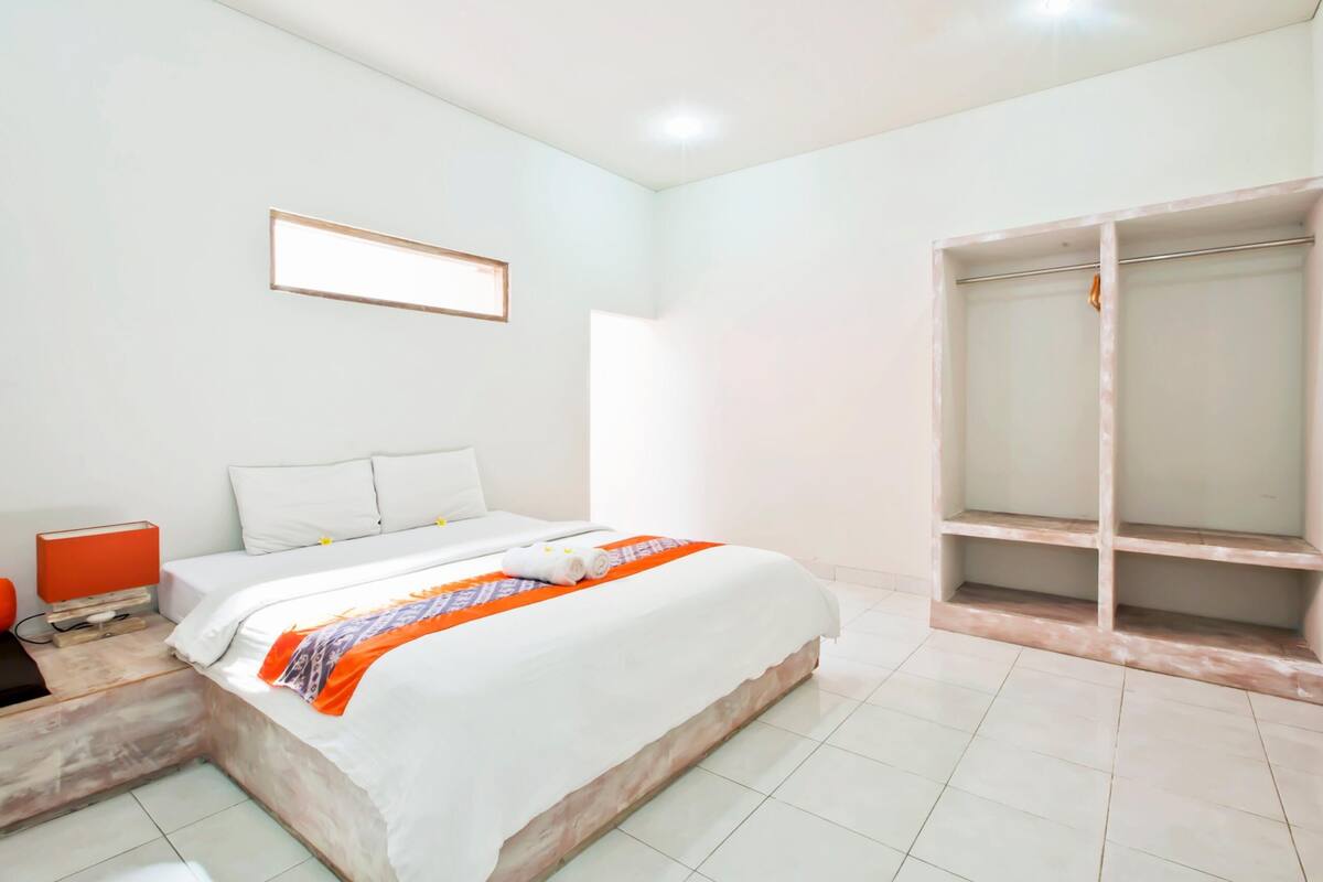 Habitación de hotel con cama, armario, una mesita con lámpara y un cuadro en la pared.