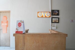 Una mesa de recepción con un cartel para la app OYO, una caja de comentarios '¿Qué te preocupa?' y un letrero de 'NO FUMAR'.
