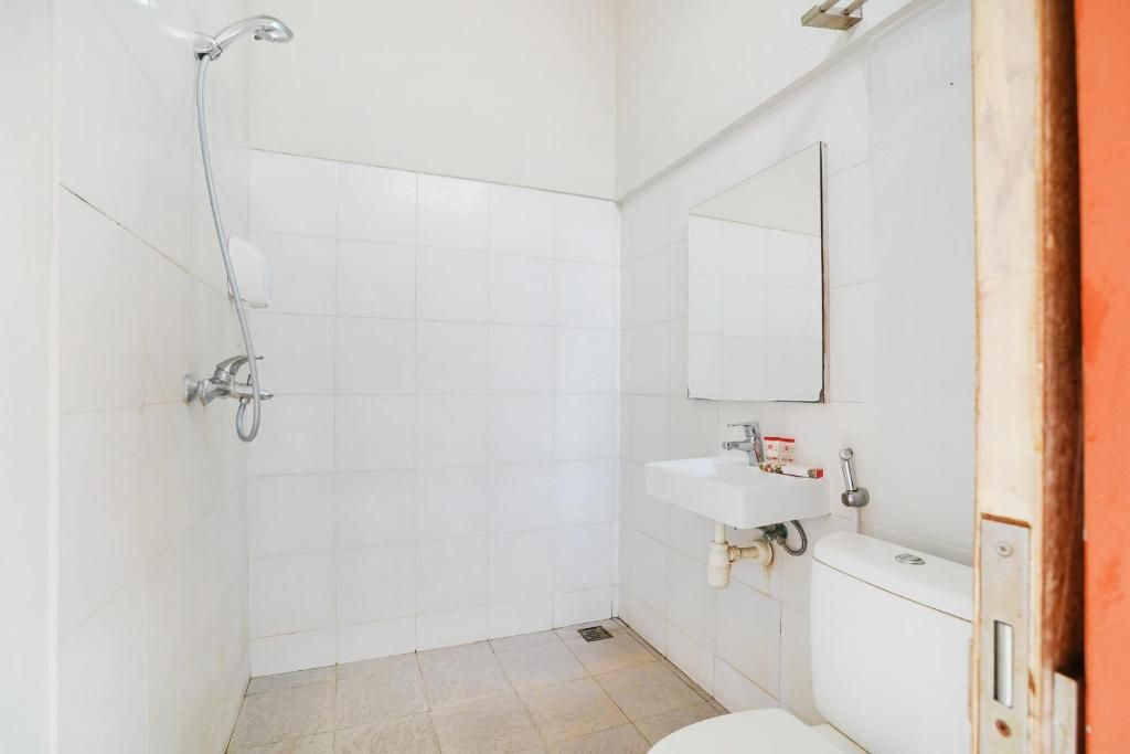 Une petite salle de bain blanche, équipée d’une douche, de toilettes et d’un lavabo.