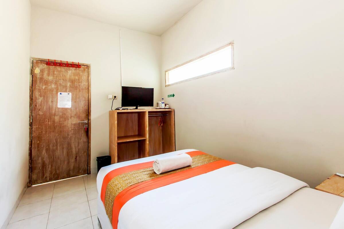 Una habitación pequeña y limpia con una cama, un armario de madera, un televisor y una ventana.