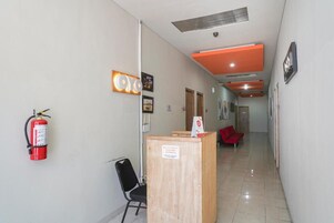 Pasillo de hotel con mostrador de recepción, extintor y una silla roja.