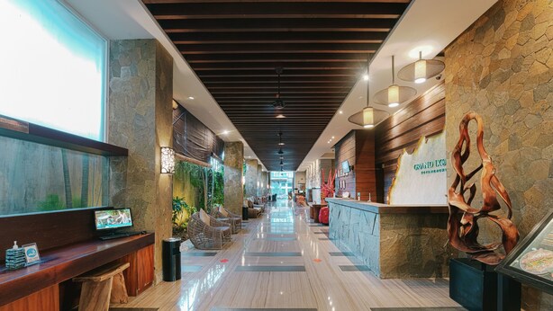 A hotel lobby with a long corridor, wooden ceiling, stone walls, and a reception desk with a wooden sculpture. - Grand Ixora Kuta Resort (Kuta)