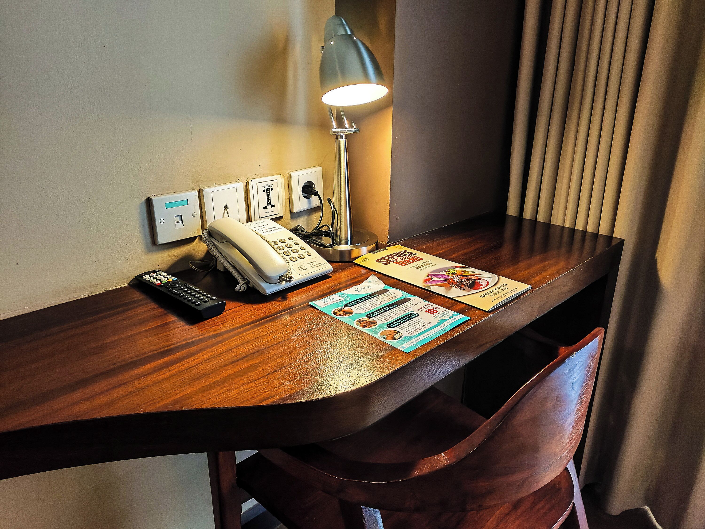 A wooden desk with a telephone, a lamp, and a menu.