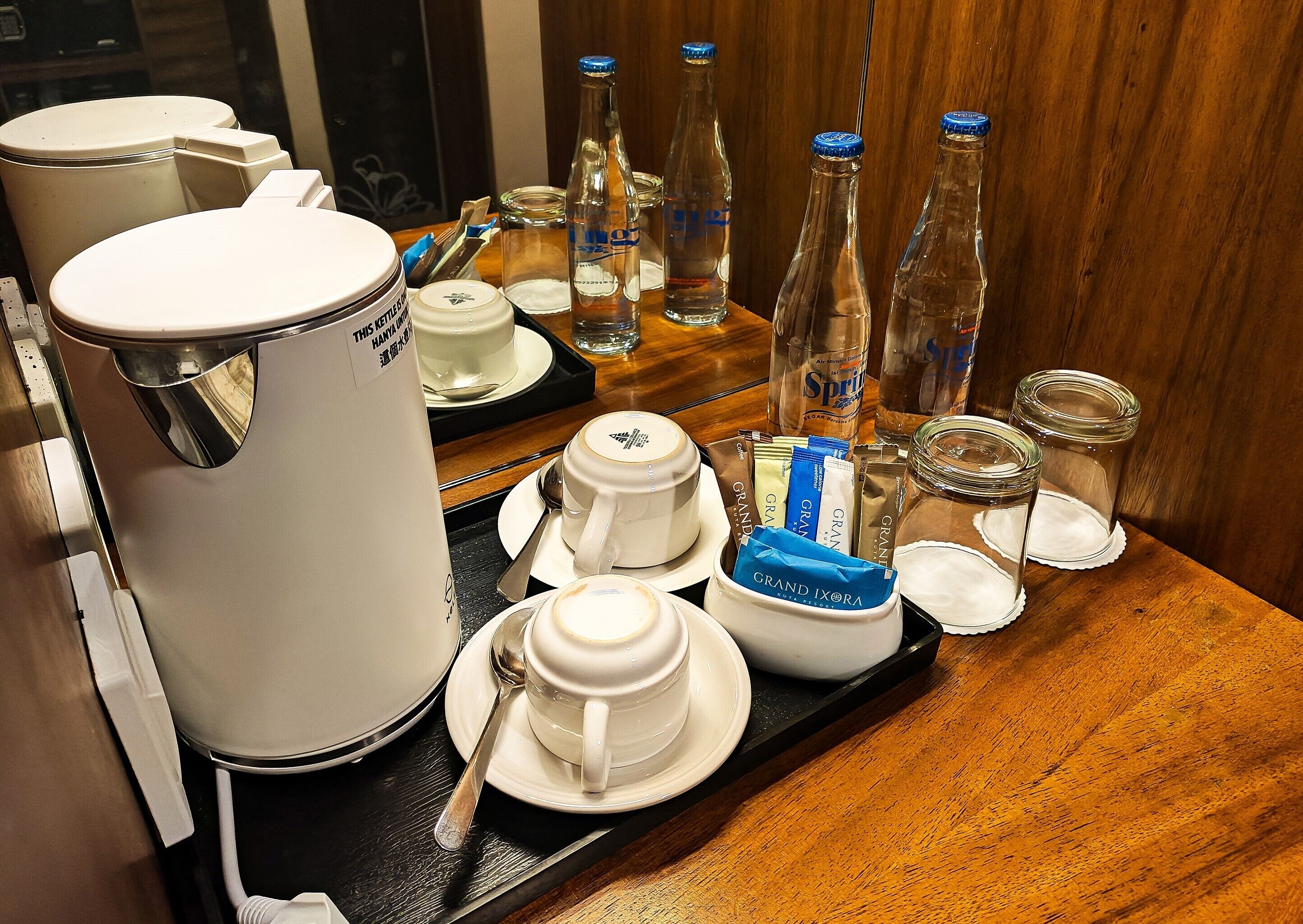 A hotel room's breakfast setup with a coffee maker, tea kettle, mugs, and bottled water.