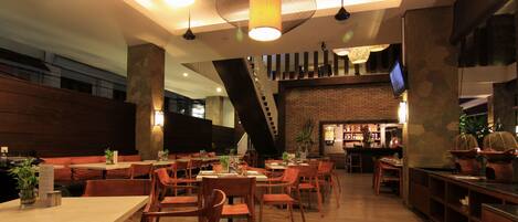 A restaurant with wooden tables and chairs, a bar area, and a staircase leading to an upper level.