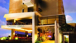 The exterior of Grand Ixora Kuta Resort with a modern architectural design, featuring a prominent entrance and outdoor seating area. - Grand Ixora Kuta Resort (Kuta)