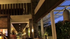 A spacious indoor area with a long corridor, wooden tables and chairs, and a bike parked near the entrance. - Grand Ixora Kuta Resort (Kuta)