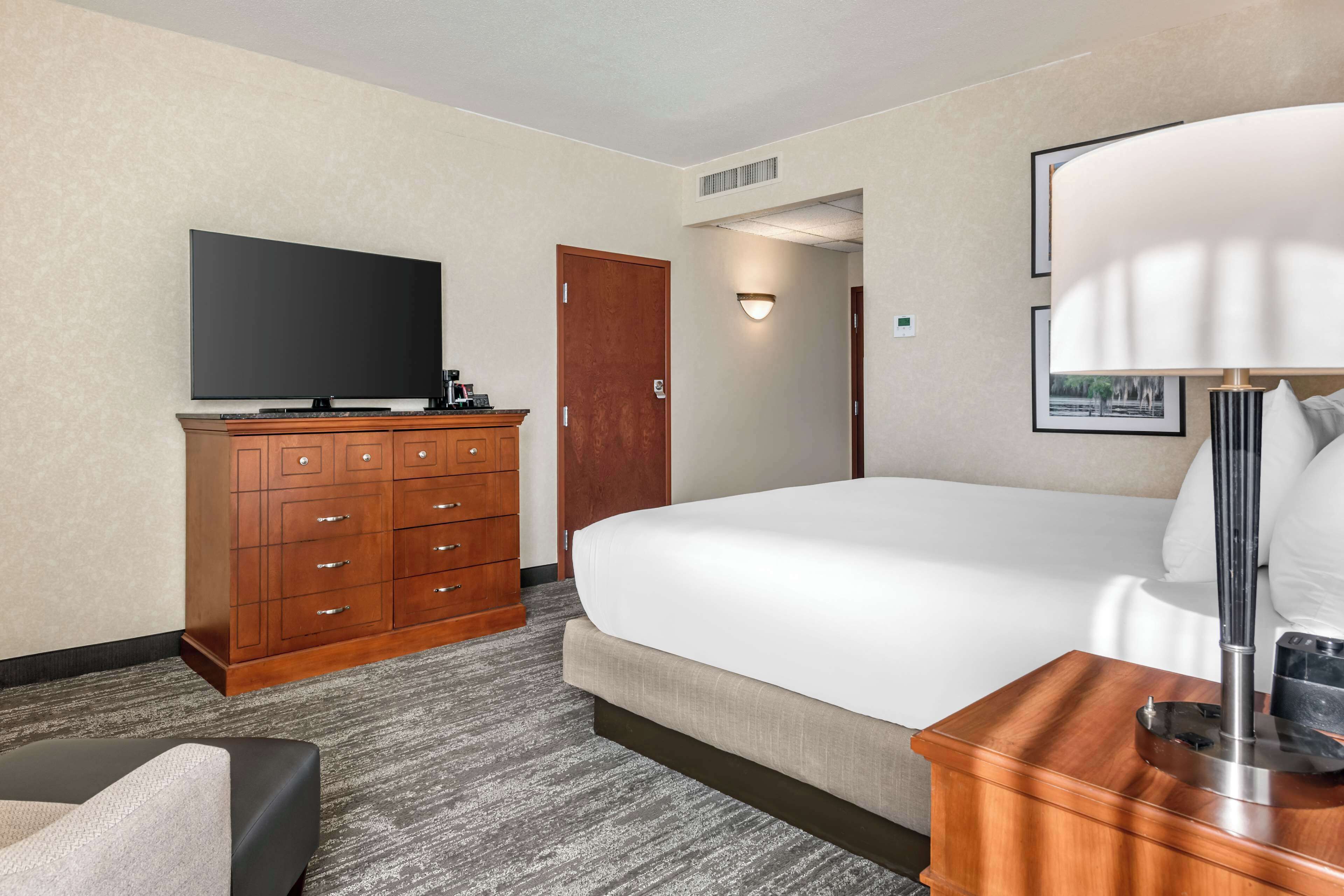 A hotel room with a large bed, a flat-screen TV, a wooden dresser, and a lamp.