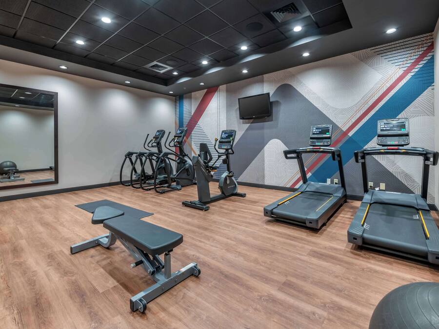 A gym with treadmills, elliptical machines, a bench, and a wall-mounted TV.