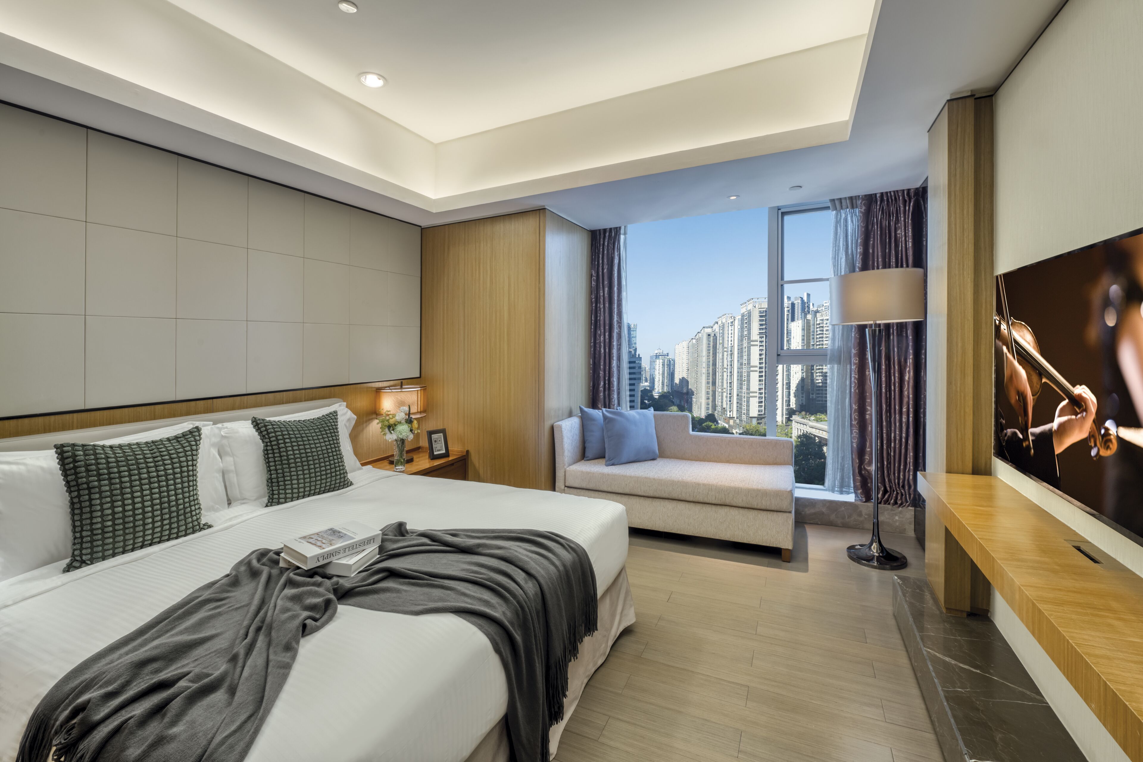 A modern hotel room with a large bed, a sofa, a TV, and a city view.