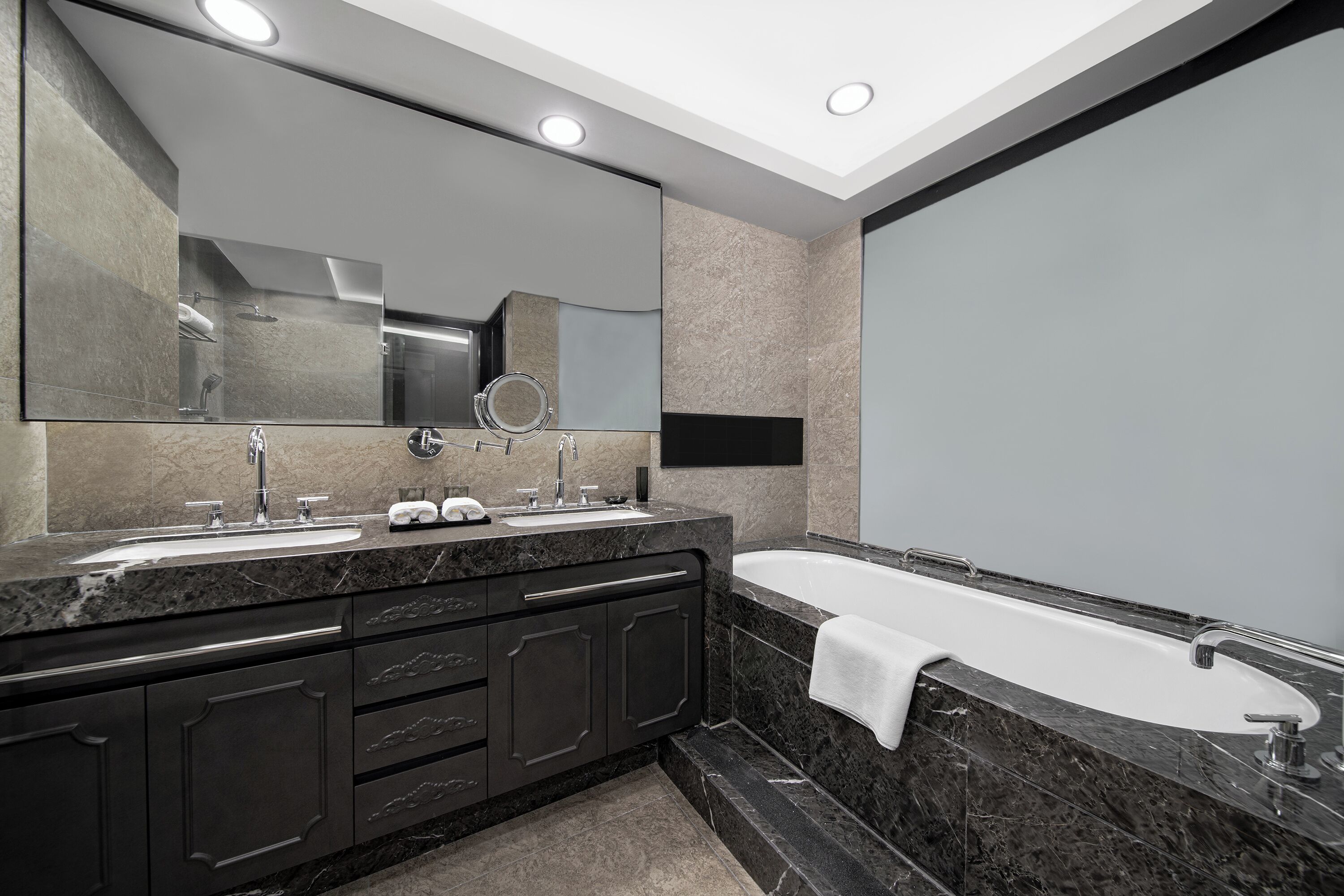 Un baño moderno con un espejo grande, dos lavamanos, una bañera y encimeras de mármol oscuro.