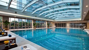A large indoor swimming pool with a glass ceiling, surrounded by seating areas and potted plants. - Ascott IFC Guangzhou (Guangzhou)