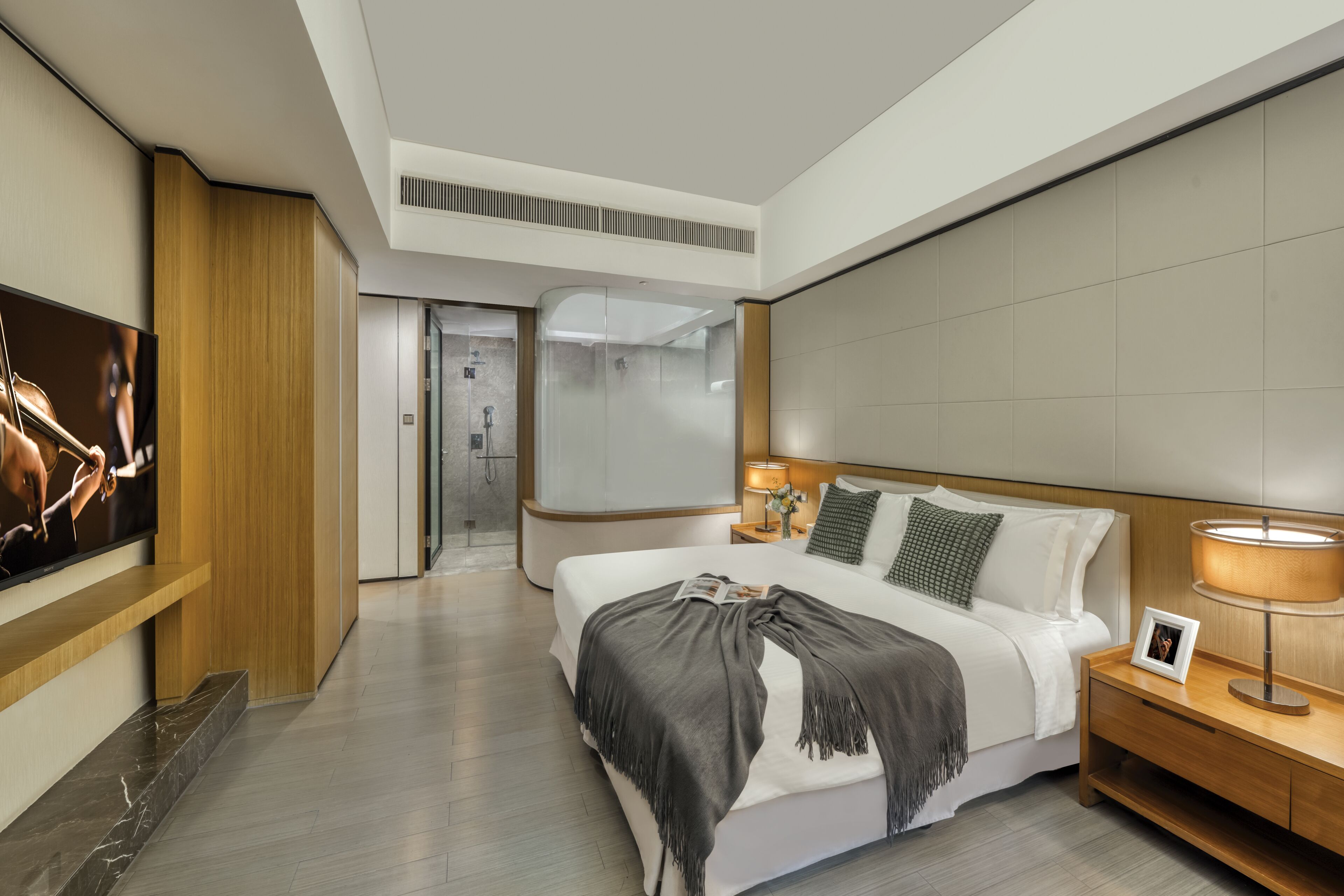 A modern hotel room with a large bed, bedside tables, a TV, and a shower area.