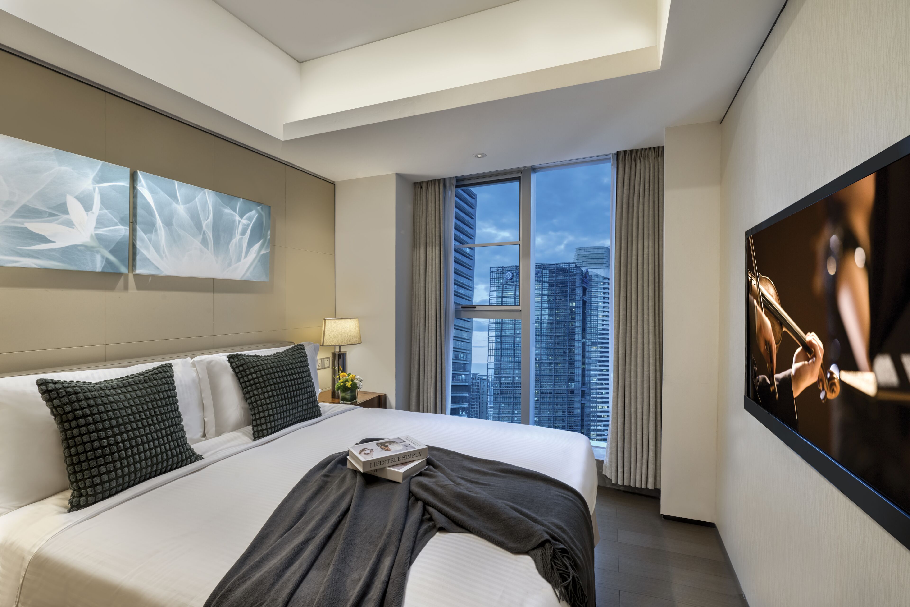Quarto de hotel moderno com uma cama grande, vista para a cidade e televisão de tela plana.