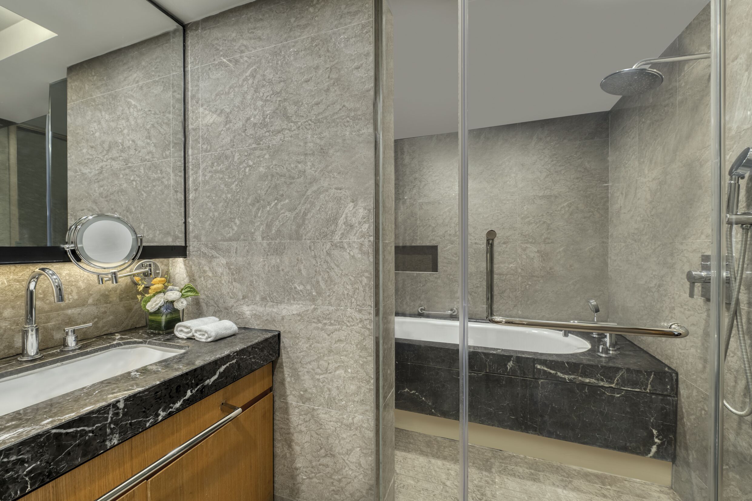 A modern bathroom with a glass shower enclosure, a sink with a marble countertop, and a mirror with a round frame.