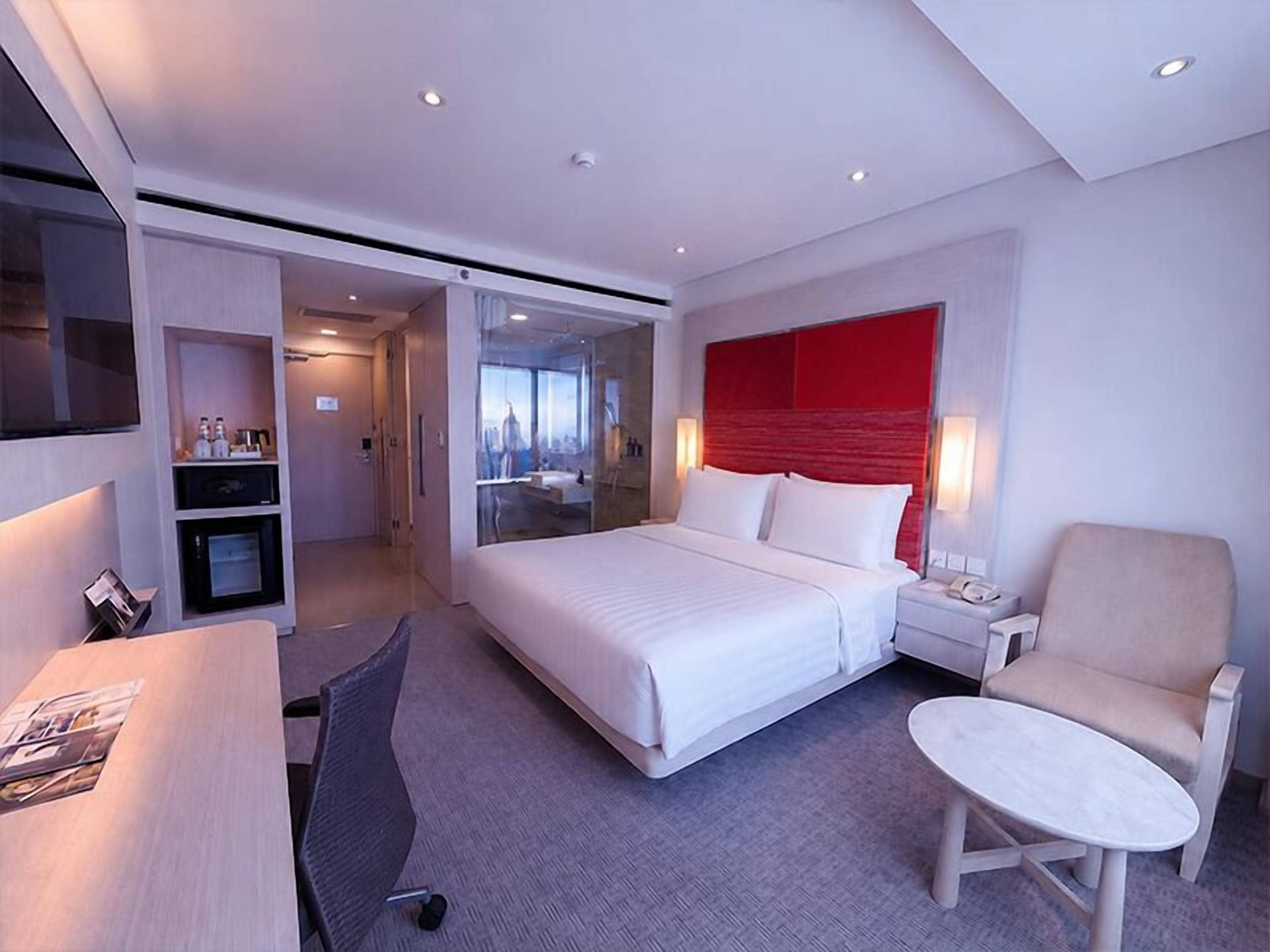 Ein modernes Hotelzimmer mit einem Bett, einem Schreibtisch, einem Sessel, einem kleinen Tisch und einem Fernseher.