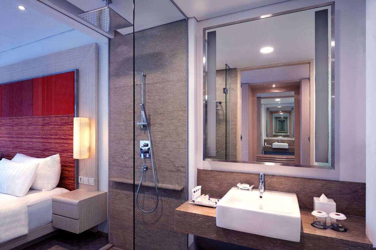 Een moderne hotelbadkamer met een douchecabine van glas, een grote spiegel en een witte wastafel.
