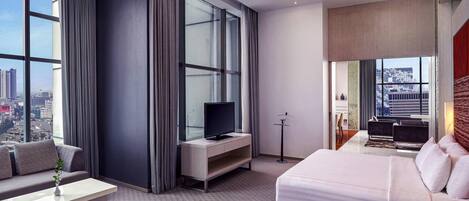 A modern hotel room with a large bed, a sofa, a TV, and a view of the cityscape.