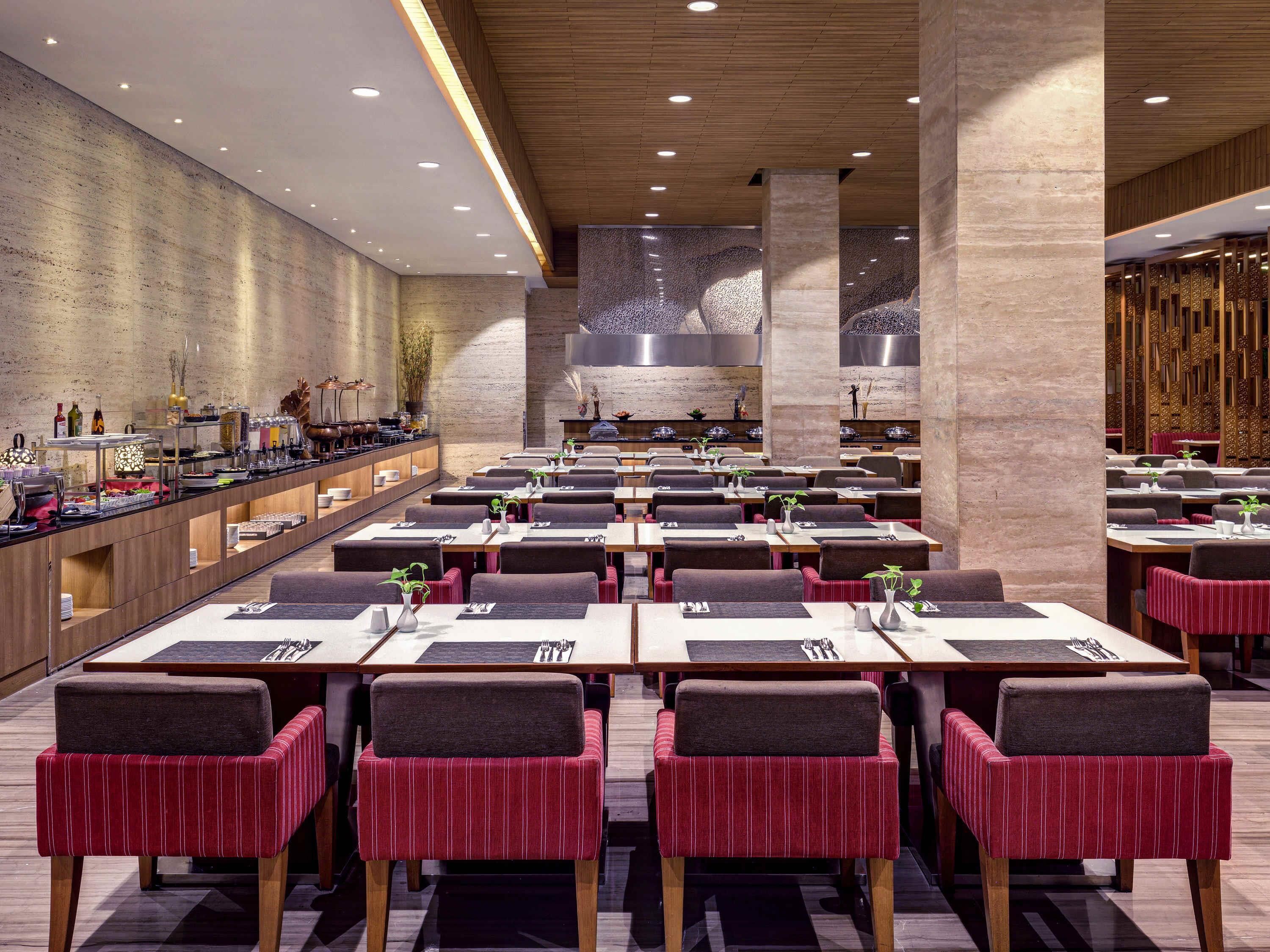 A spacious restaurant with multiple dining tables and booths, a buffet area on the left, and a large stone wall in the background.