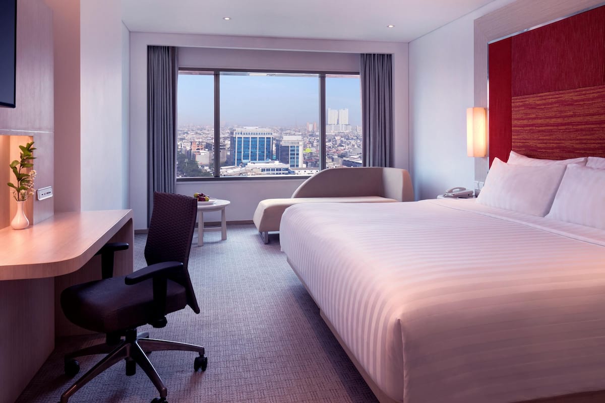 Une chambre d’hôtel équipée d’un lit, d’un bureau, d’une chaise et offrant une vue sur le paysage urbain.