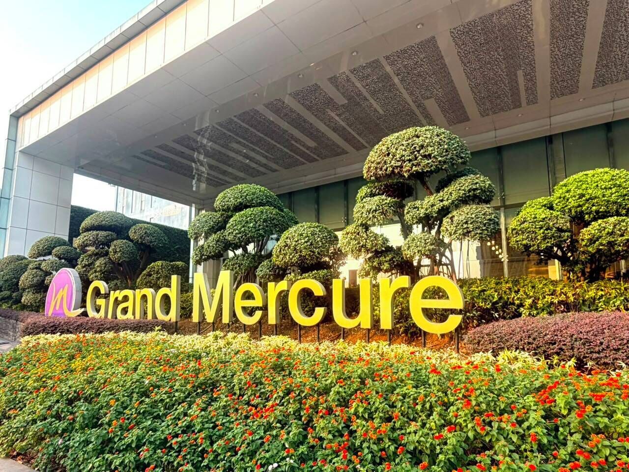 Un edificio con el letrero 'Grand Mercure' y jardines topiarios bien cuidados al frente.