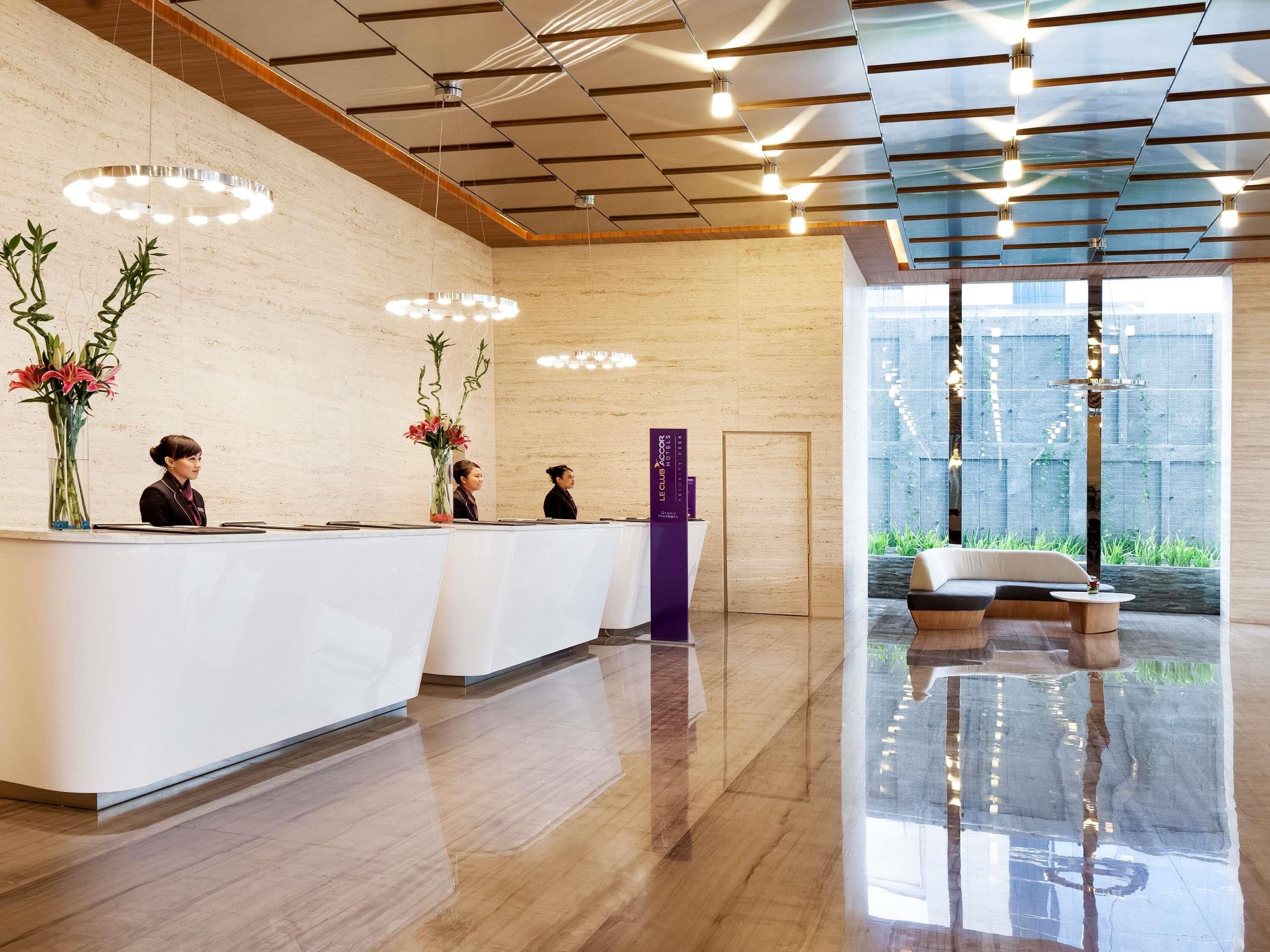 A hotel reception area with a modern design, featuring a reception desk, a seating area with a sofa, and a large window providing a view of the outdoors.