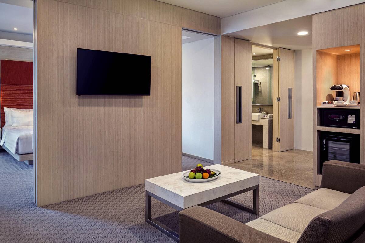 Een moderne hotelkamer met een flatscreen televisie, een eettafel met fruit, een sofa en een kitchenette.
