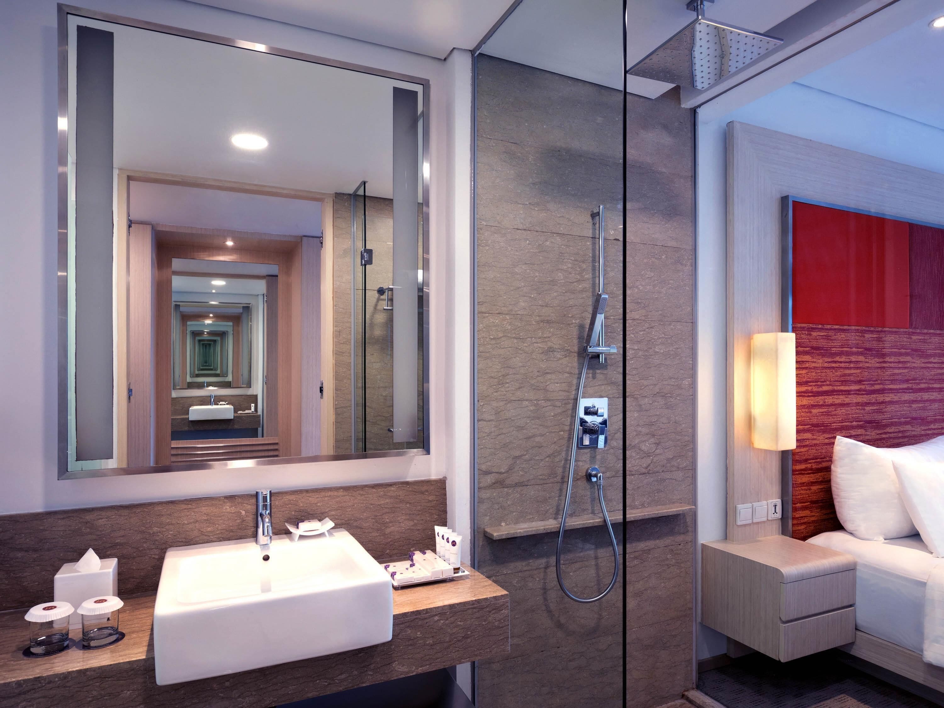 Une salle de bain moderne avec un grand miroir, un lavabo, une douche et une table de chevet avec une lampe.