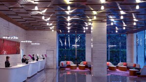 Un hall d’hôtel moderne doté d’un comptoir d’accueil, d’un espace salon et de grandes fenêtres offrant une vue sur la verdure.