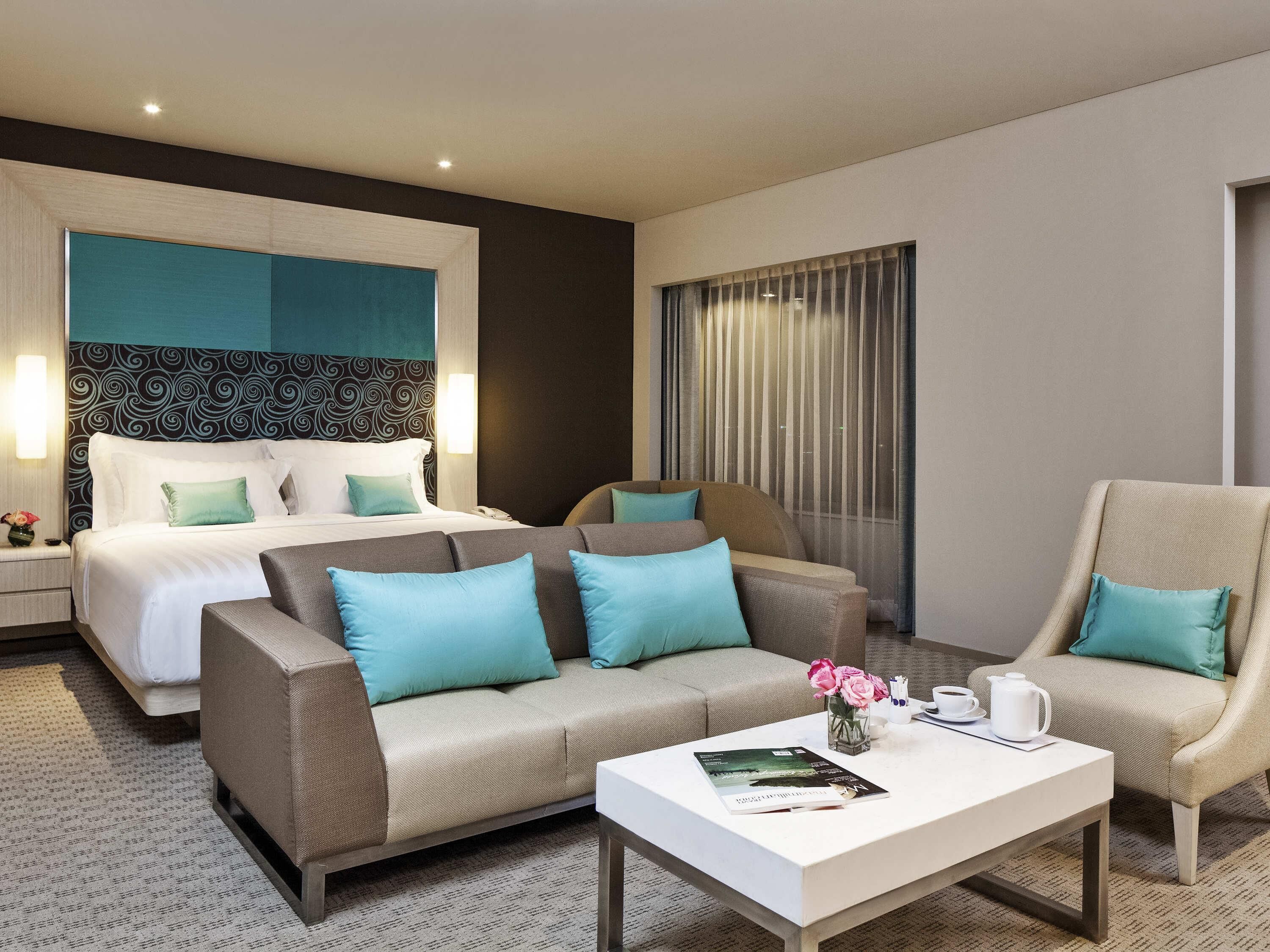 A hotel room with a bed, two sofas, a coffee table, and a window with curtains.