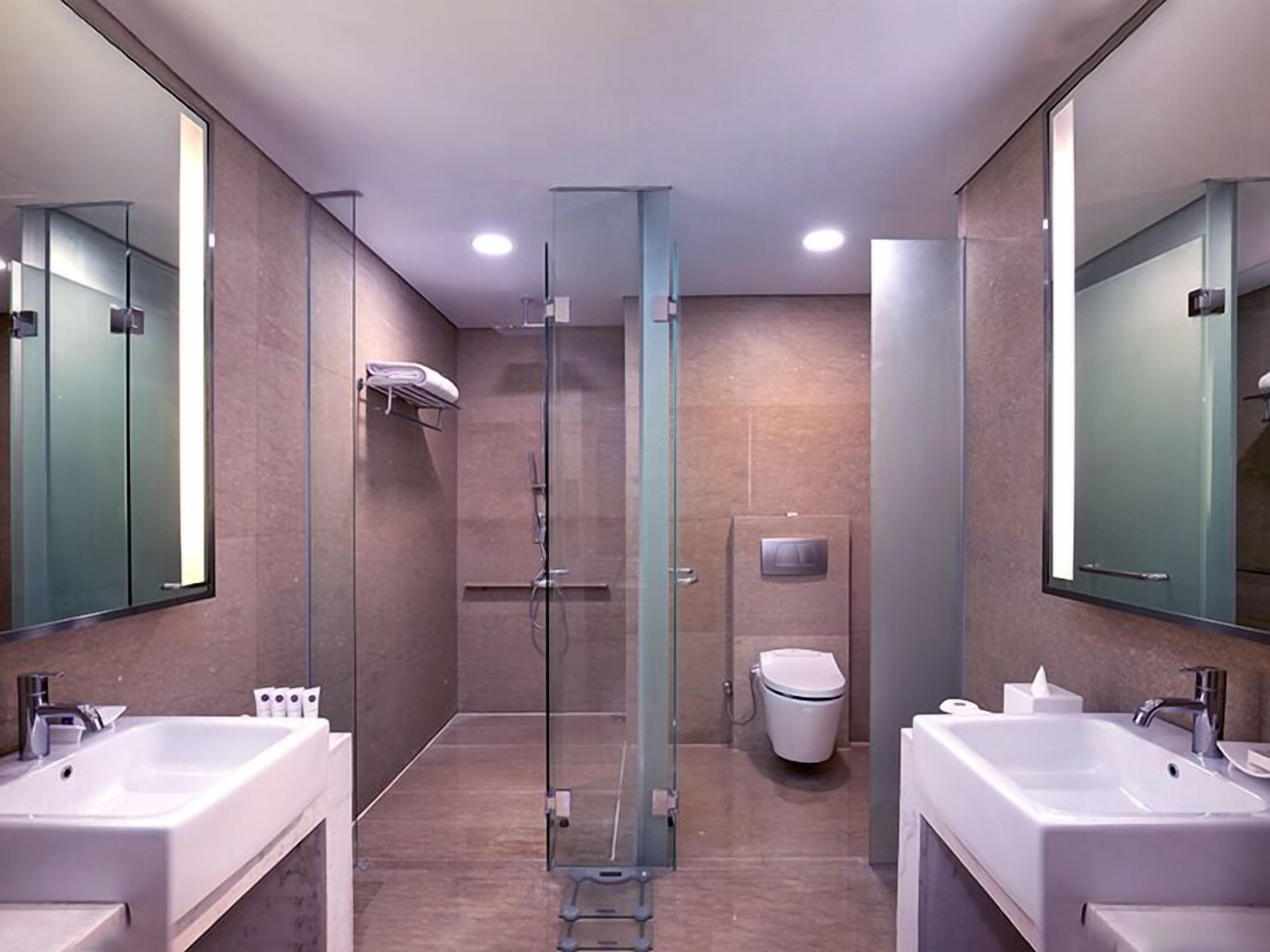 Un baño moderno con dos lavamanos, cabina de ducha con mampara de vidrio y un inodoro.