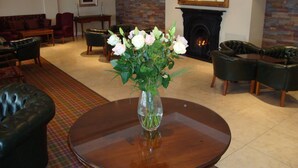 A living room with a fireplace, leather furniture, and a vase of flowers on a round table. - Ard Ri House Hotel (Tuam)
