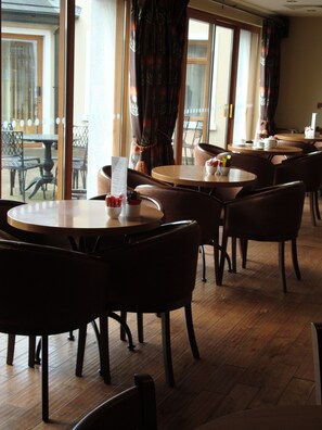 A restaurant with round tables and chairs, a menu stand, and large windows with curtains.