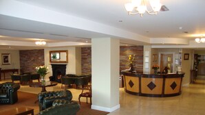 A lobby with leather sofas, a reception desk, a fireplace, and a tiled floor. - Ard Ri House Hotel (Tuam)