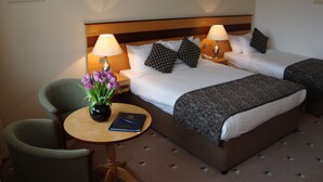 A hotel room with two beds, a chair, a small table with a vase of flowers, and a book. - Ard Ri House Hotel (Tuam)