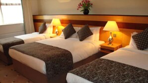 A hotel room with two beds, each with a patterned bedspread, a nightstand with a lamp, and a vase with flowers on the headboard.
