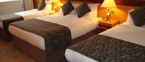A hotel room with two beds, each with a patterned bedspread, a nightstand with a lamp, and a vase with flowers on the headboard.