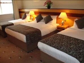 A hotel room with two beds, each with a patterned bedspread, a nightstand with a lamp, and a vase with flowers on the headboard.