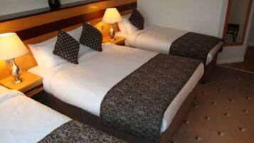 Habitación de hotel con dos camas, cada una con almohada y lámpara. Hay un florero con flores en la pared y una alfombra estampada en el suelo.