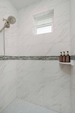 Un baño con ducha, ventana y estante con artículos de aseo.