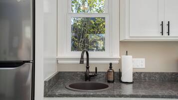 A kitchen with a stainless steel refrigerator, a dark granite countertop, a single-basin sink, a faucet, a bottle of hand soap, and a roll of paper towels.