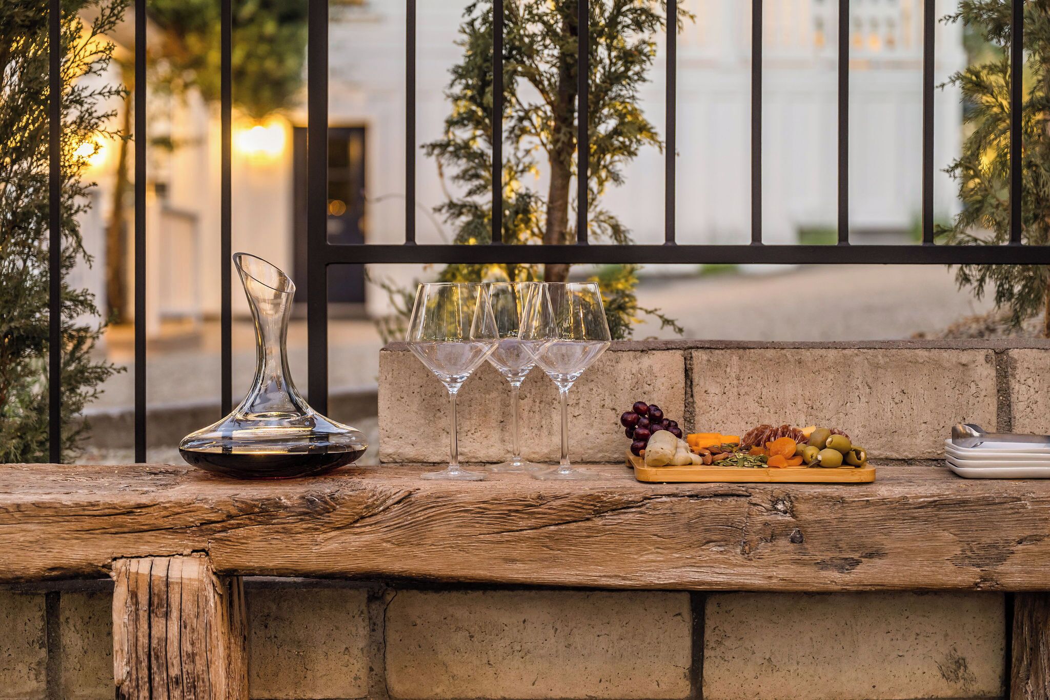 A wooden table with a wine decanter, three wine glasses, and a fruit platter.