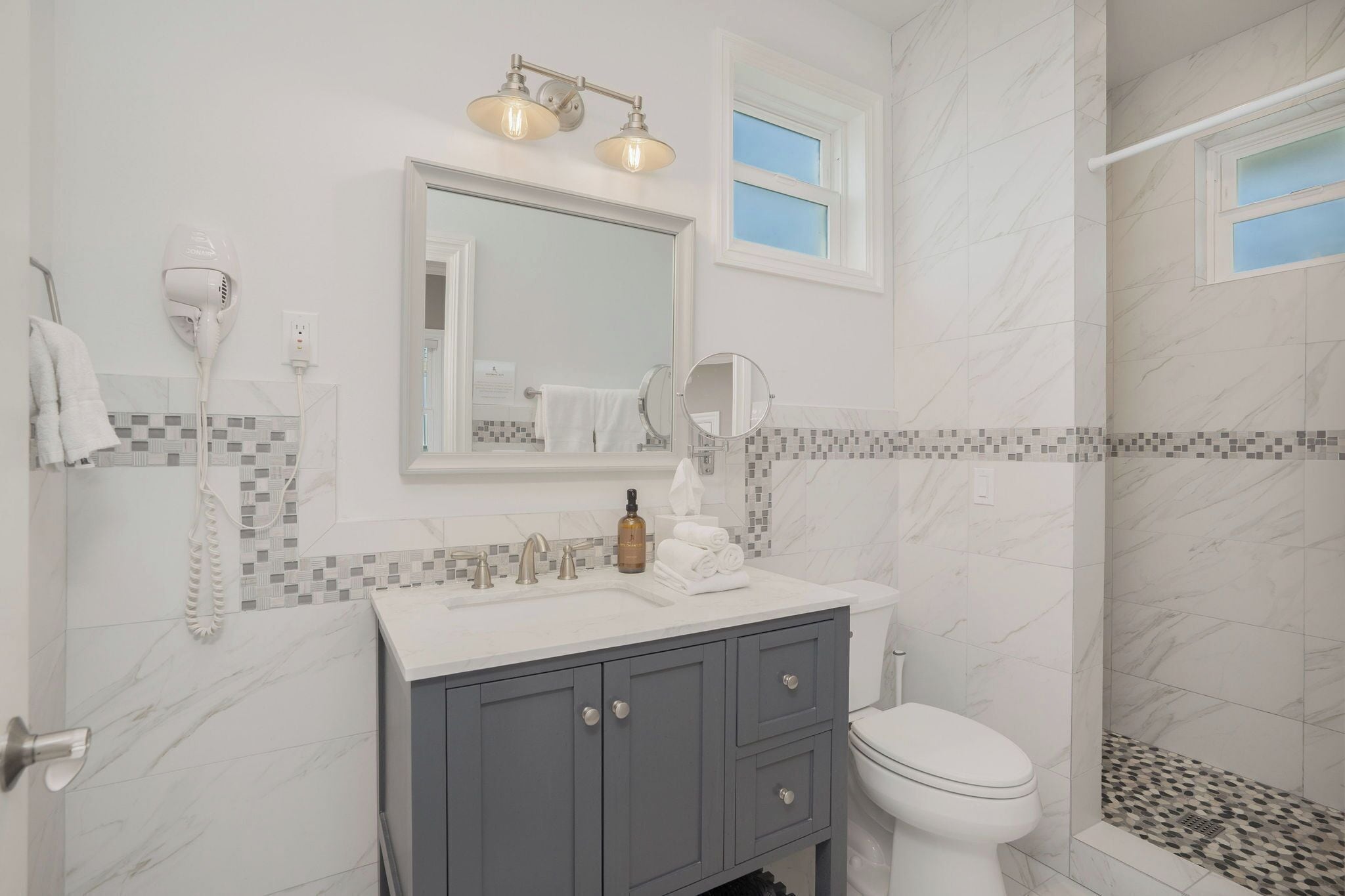 A bathroom with a white sink, vanity, and toilet. There is a shower with a glass door and a tiled shower floor.
