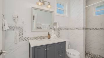 A bathroom with a white sink, vanity, and toilet. There is a shower with a glass door and a tiled shower floor.